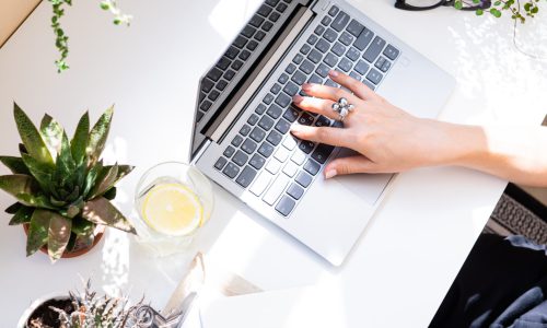 Woman’s hands on laptop keyboard, writing in notepad Woman's hands on laptop keyboard, writing in notepad, cozy workplace with home plants closeup
